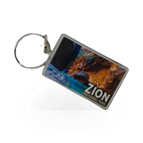 Impact Photographics compass keychain featuring a small, metal compass pendant with a woven strap, ideal for travel and outdoor use.
